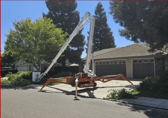 Spider crane reaching over house for tree trimming